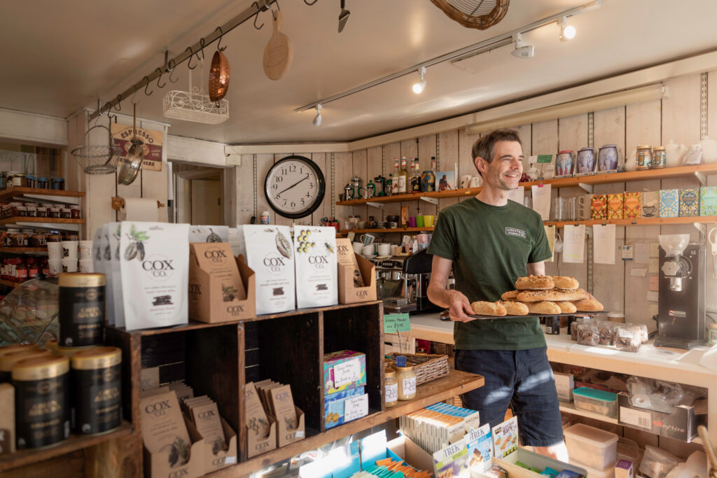 (c) Christopher Ison Photography – Comestibles Standard Membership photo ISON_200529_Midhurst_546314 Interior of Comestibles delicatessen and cafe in Midhurst with a staff member holding a tray of fresh bread.