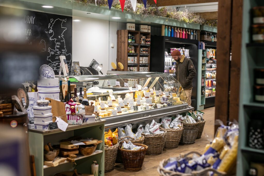 (c) Cowdray – 2023-George Gunn-1088 A view of the cheese counter with a customer inside the Cowdray Farm Shop in Midhurst, West Sussex.