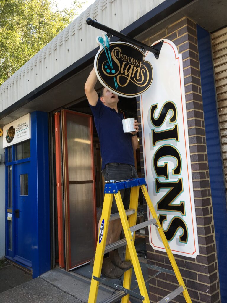 (c) Osborne Signs Ltd A staff member of Osborne Signs Ltd, painting the sign of Osborne Signs Ltd