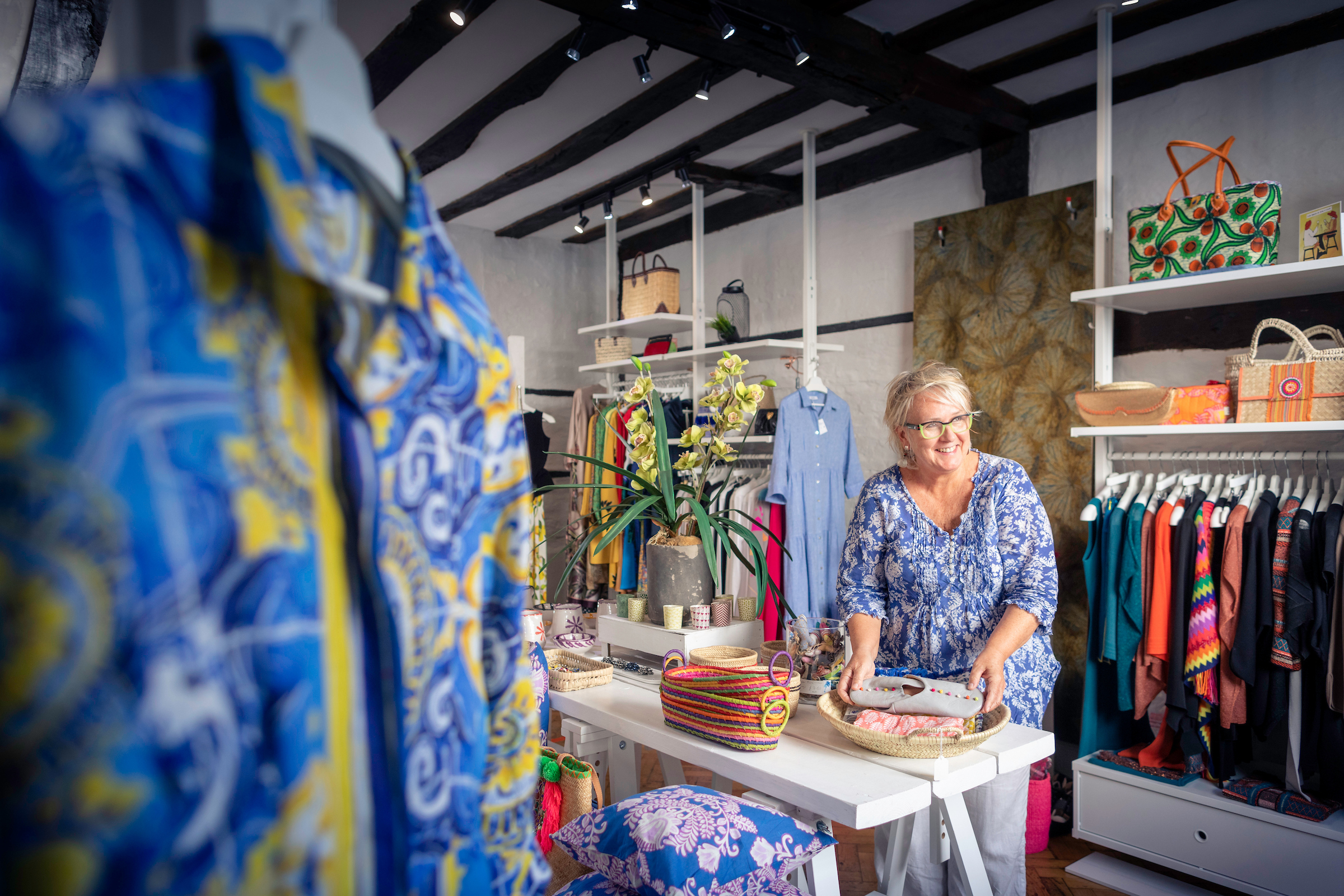 A staff member of the Sussex House Boutique shop behind the counter next to a range of colourful women's clothing.