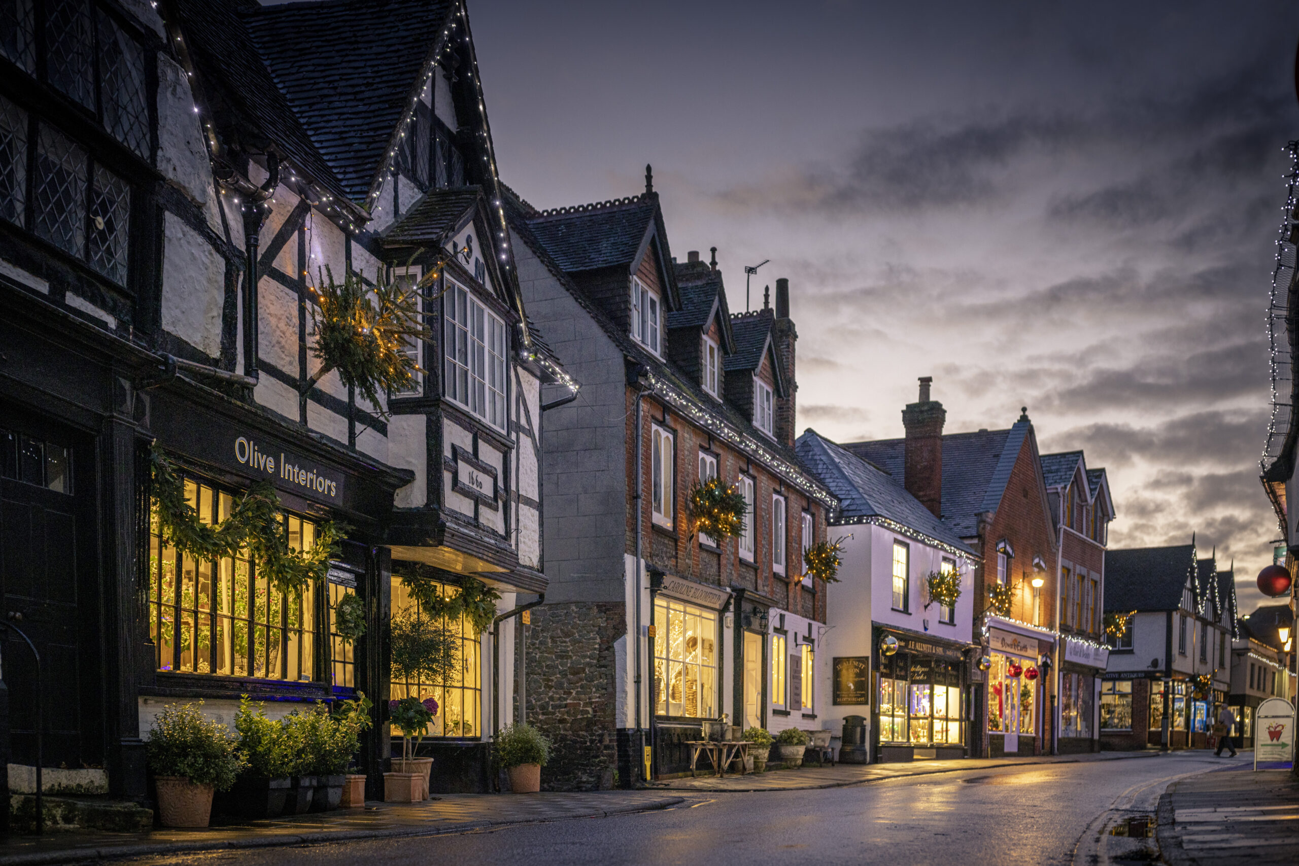 Shop fronts of West Street in Midhurst at dusk with Christmas lights and decorations.