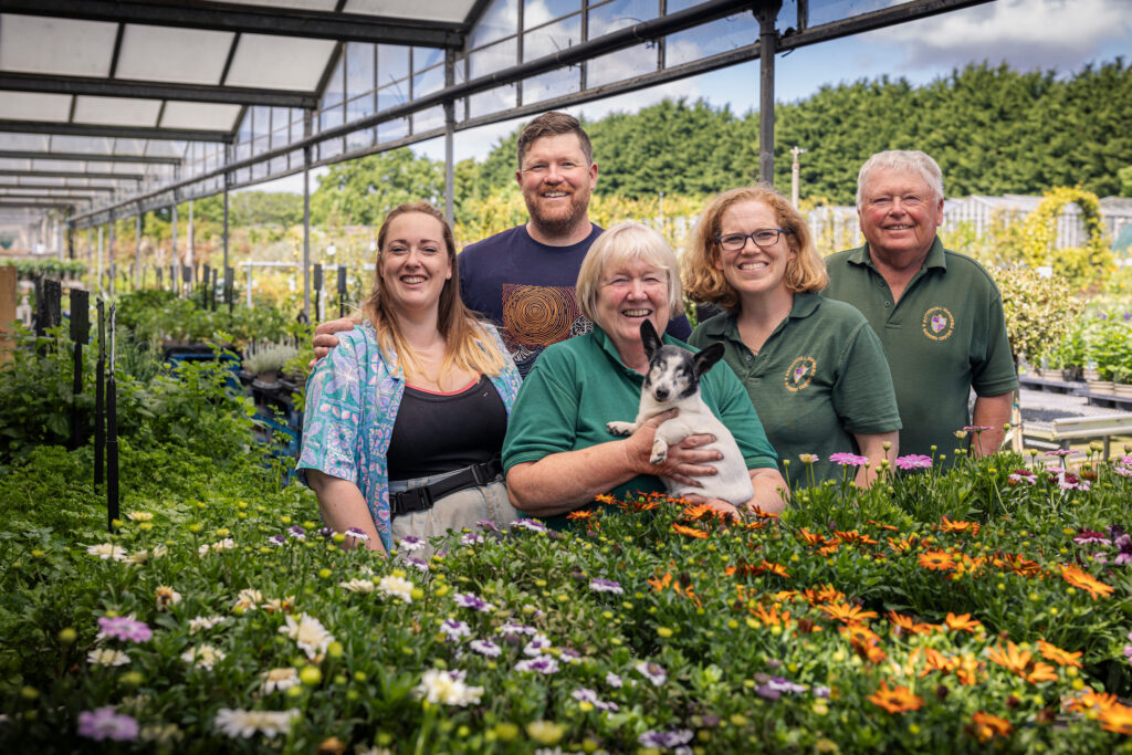 (c) Christopher Ison Photography – ISON_240515_RNGC_5319 Five happy staff members of Rotherhill Nurseries and Garden Centre and a dog surrounded by growing flowers.