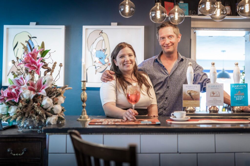 Two staff members behind the bar of The Swann Inn in Midhurst. One is holding a wine glass.